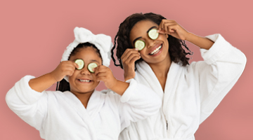 Mother and daughter in white spa robes with cucumber slices over their eyes, promoting the Fire & Ice Full Body Massage